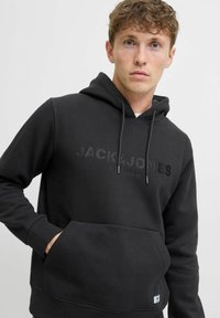 Felpa nera con cappuccio in tessuto morbido, dotata di tasca frontale, cappuccio regolabile con cordoncino e logo in rilievo "JACK & JONES PREMIUM" sul petto.