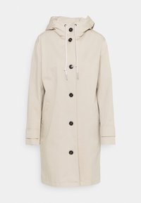 Beige gewatteerde jas met capuchon, voorzien van een voorplooibare sluiting met zwarte knopen, zijzakken en verstelbare trekkoorden aan de capuchon en manchetten.