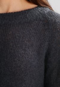 Pull léger gris foncé en tissu pelucheux et texturé avec un large décolleté et des accents côtelés au niveau du col.