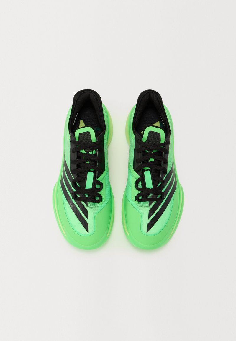 Zapatillas de deporte verde brillante con parte superior de malla, acentos negros y una suela de goma lisa. Los cordones son negros; líneas de diseño notables en los laterales.