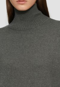 Pull gris à col montant en tricot côtes. Présente un col haut et une texture lisse, offrant une apparence ajustée.
