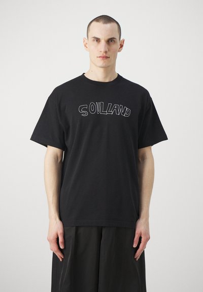 T-shirt en coton noir avec le texte "SOULLAND" en blanc entouré sur la poitrine. Manches courtes et col rond, coupe décontractée, design minimaliste.