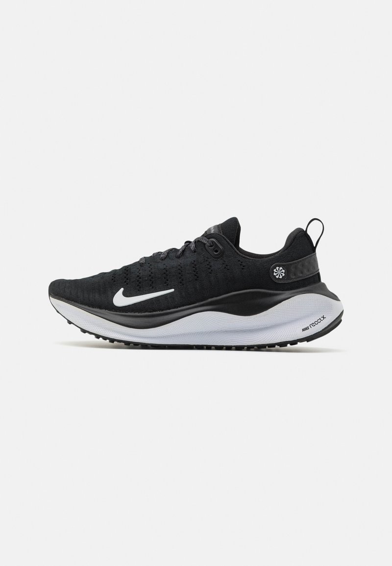 Chaussure de sport noire avec une tige texturée, logo swoosh blanc, semelle intermédiaire noire et blanche, et semelle extérieure à motif. Présente une languette au talon.