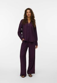 Ensemble deux pièces violet comprenant une chemise à manches longues à boutons et un pantalon large, fabriqué dans un tissu texturé avec des poches latérales.