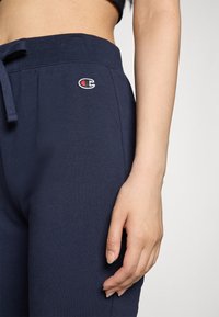 Marineblaue Sweatpants aus weichem Stoff mit elastischem Bund und Kordelzug, ausgestattet mit einem kleinen gestickten Logo an der Hüfte.
