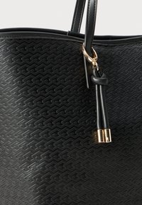 Black textured leather handbag with geometric pattern, featuring double handles and leather tassels with gold metal tips.