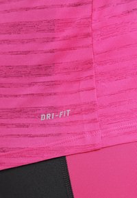 Detailní záběr na růžové sportovní tričko s viditelným štítkem "DRI-FIT", doplněné černými a růžovými legínami.