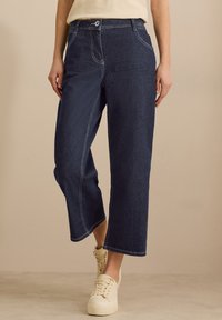 Pantalones vaqueros de pierna ancha en azul oscuro, confeccionados con denim, que presentan costuras de contraste, bolsillos y un cierre clásico con botón en la cintura.
