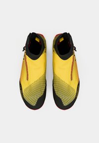 Zapatos de escalada amarillos con un diseño texturizado, acentos en negro y un cremaller lateral. Cuentan con un ajuste ceñido y patrones contrastantes para mayor agarre.