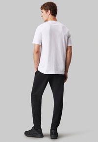 Maglietta in cotone bianca, maniche corte, colletto tondo. Abbinate a pantaloni jogger neri, tasca laterale, caviglie elastiche e scarpe sportive nere.