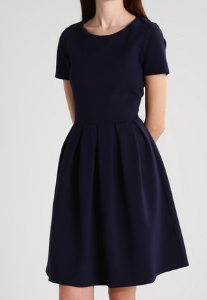 Granatowa sukienka z krótkim rękawem, okrągłym dekoltem, dopasowanym gorsetem i rozkloszowaną spódnicą. Wykonana z gładkiego materiału z plisami w talii.