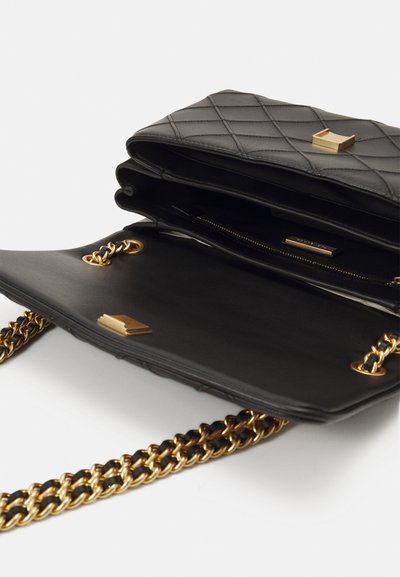 Black quilted leather handbag with a gold chain strap, featuring a zippered compartment and a gold accent on the flap for detail.