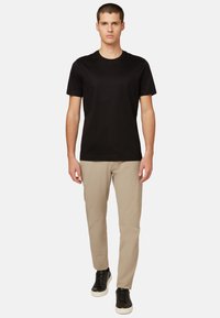 Sort bomulds t-shirt parret med beige slim-fit bukser og sorte sneakers. Modelen står oprejst mod en hvid baggrund.