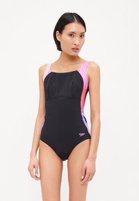 Maillot de bain noir avec des panneaux latéraux roses et violets, doté d'un décolleté carré et de larges bretelles. Logo présent sur le bas à droite.