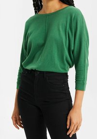 Grön lättviktsstickad tröja med bred båtöppning, trekvartsärmar och avslappnad passform, matchad med svarta högmidjade jeans.