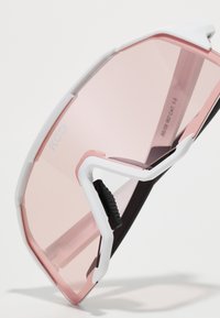 Lunettes de soleil au design élégant, monture blanche et noire, verres teintés en rose et plaquettes de nez ajustables. Présente un logo de marque bien visible.