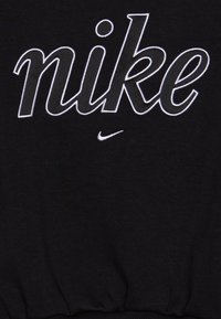 Melna sporta jaka ar lielu baltu izšūtu "nike" logotipu un nelielu baltu "swoosh" apakšā. Auduma struktūra izskatās mīksta un gluda.