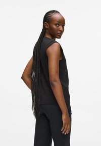 Mustamata ilma varrukat topp ümardatud õlgade õmblustega, pehme kangas ja lahti lõige. Taust on lihtne valge, rõhutades riietust.