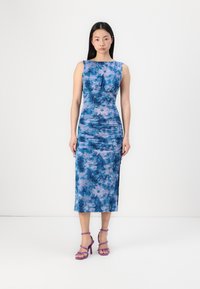 Robe florale bleue cintrée avec des détails froncés, sans manches, longueur genou, associée à des talons strappy violets. Texture du tissu lisse.