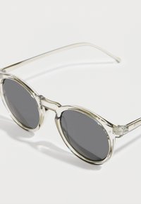 Στρογγυλά γυαλιά ηλίου με διαφανές σκελετό, σκούρους γκρι φακούς και διαφανείς βραχίονες. Ομαλή υφή με ελάχιστες λεπτομέρειες εξοπλισμού.