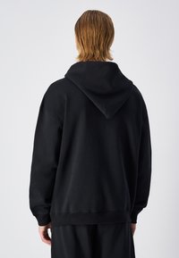 Felpa nera oversize realizzata in tessuto morbido. Presenta un grande cappuccio, spalle scese e polsini e fondo a costine. Design semplice e minimale.