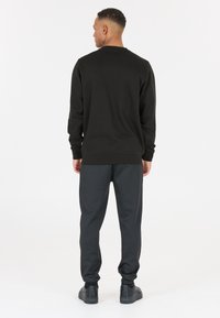 Svart stickad tröja med långa ärmar, rundad hals och ribbad nederkant, matchad med mörka joggingsbyxor och svarta sneakers, sedd bakifrån.