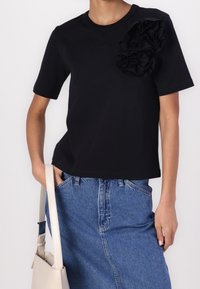 Camiseta negra de manga corta, con volantes de tela tridimensional en el lado izquierdo. Combinada con una falda de mezclilla azul clara.