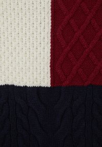Knit fabric featuring a color-block design: cream, red, and navy sections, with textured patterns and cables in red and navy.