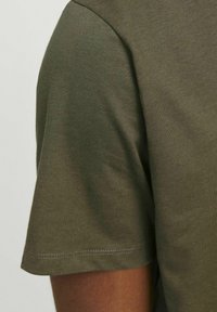 Olivno zelena kratka majica s kratkimi rokavi, izdelana iz mehkega materiala, s krožnim izrezom in ravnim robom ter subtilnimi šivi.