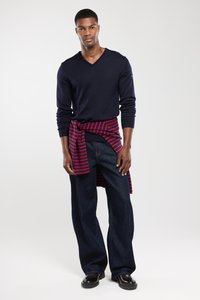 Marineblauer V-Ausschnitt-Pullover, rot-blau gestreiftes Hemd, das um die Taille gebunden ist, lockere dunkle Jeans und schwarze Schuhe. Einfaches Design mit minimalen Akzenten.