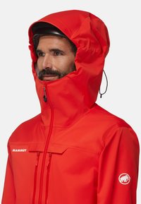 Rote wasserdichte Jacke mit hohem Kragen, verstellbarem Kapuze, vorderem Reißverschluss und zwei Reißverschlusstaschen. Mit Markenzeichen am Ärmel.