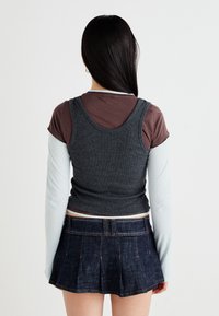 Gray tank top layered over a brown shirt, paired with a dark denim pleated mini skirt. The materials have a soft texture and relaxed fit.