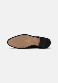 Pantof de piele neagră cu un upper neted, vârf ascuțit și talpă din cauciuc bej. Prezintă cusături detaliate pe margine și o talpă texturată.