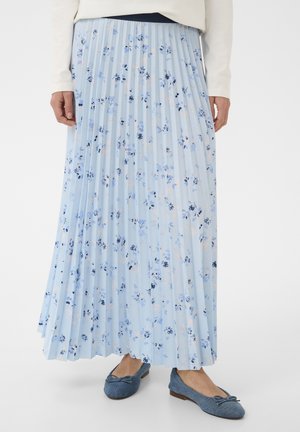 Jupe maxi plissée bleu clair avec petit motif floral bleu, associée à des ballerines bleues et un haut à manches longues blanc.