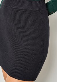 Gonna nera a maglia con una texture a coste, caratterizzata da un design aderente e una vita liscia. Il dettaglio della cucitura laterale aggiunge un interesse sottile.