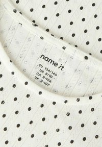 Hvid stof-T-shirt med vandrette striber og sorte polkaprikker, med rund hals og plejemærke. Blød tekstur.