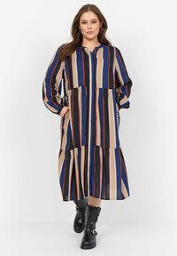 Robe longue à rayures dans des teintes marine, noire, beige et rouille, dotée d'une fermeture à boutons, d'une jupe froncée et de manches longues, portée avec des bottines noires.