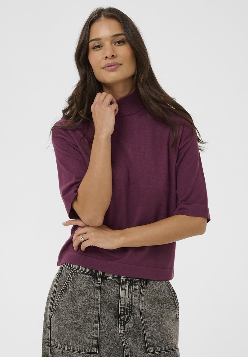 Short-sleeve purple top with a high neck, made from soft material; paired with high-waisted faded gray jeans with pockets.