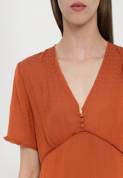 Vestido de color óxido con escote en V, mangas cortas y tres botones como acento en la zona del cuello; tejido texturizado con un patrón sutil.