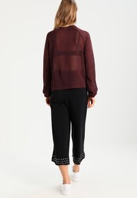 Pull transparent bordeaux à manches longues avec un panneau arrière. Pantalon noir avec ourlet festonné et accents à pois aux poignets. Baskets blanches.