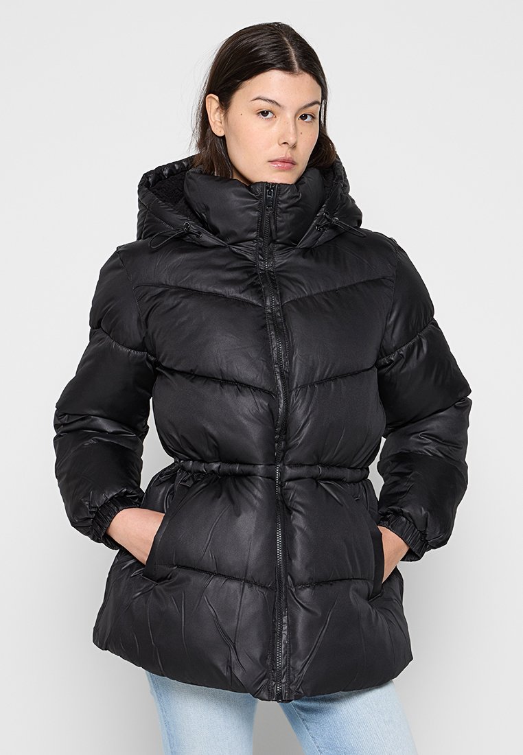 Veste matelassée noire avec capuche, taille élastique, fermeture éclair et poches latérales. Dotée d'un design matelassé et d'une texture lisse et brillante.