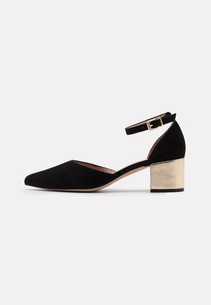 Black suede high-heeled shoe with a pointed toe, ankle strap, and a metallic gold block heel. Smooth texture and minimalistic design.