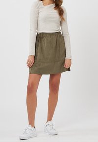 Jupe en daim khaki avec une taille élastique, de forme évasée, et un ourlet juste au-dessus du genou, associée à un haut léger à manches longues et des baskets.