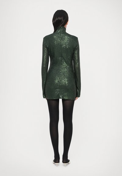 Zöld flitteres dzsekiruha magas nyakkal és hosszú ujjakkal, testhezálló szabással és rövid szegéllyel. Feketén harisnyával párosítva.