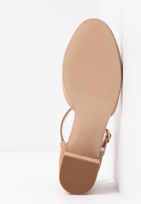 Sandale en suede nude avec une semelle plate, dotée d'une seule sangle à la cheville et d'une conception à bout fermé. Texture lisse avec un style minimaliste.