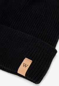 Cappello a maglia nero a coste con polsino risvoltato, caratterizzato da una piccola etichetta in pelle marrone con la "W" in rilievo. Tessuto morbido, materiale caldo.