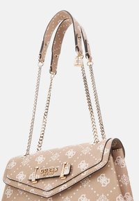 Beige Guess håndtaske med hvidt monogramprint, guld kæde-stropper og en lille guld hængelås charme på håndtaget.