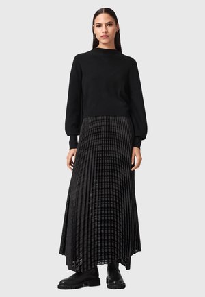 Maglione nero con scollatura rotonda e maniche a sbuffo abbinato a una gonna lunga plissettata nera con motivo a rete e stivali alla caviglia.