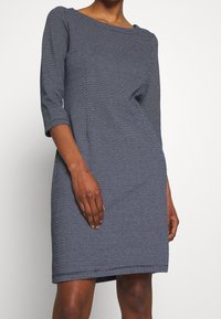 Marinblå klänning med en strukturerad mönster, trekvartsärmar och rund halsringning. Lätt figursydd form, knälång modell.