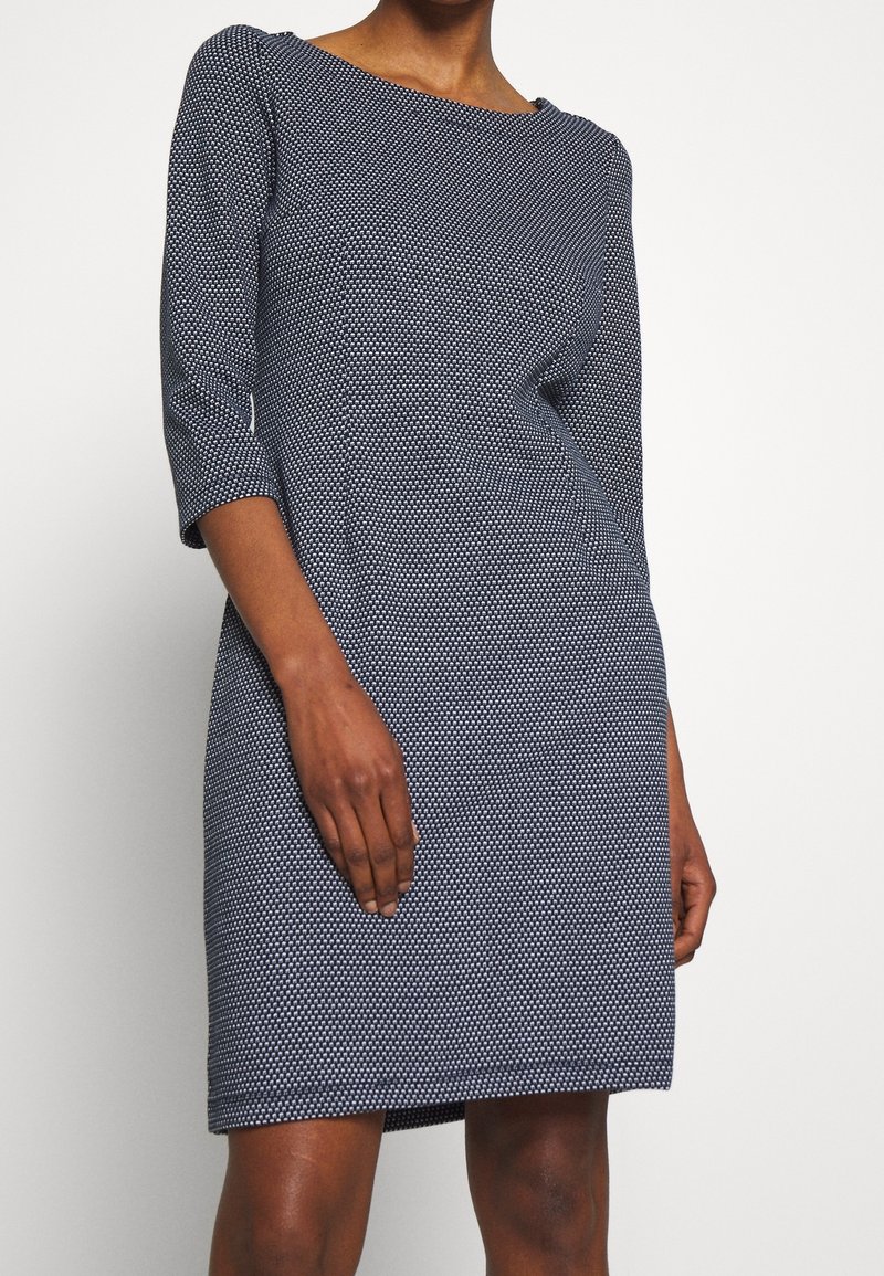 Marinblå klänning med en strukturerad mönster, trekvartsärmar och rund halsringning. Lätt figursydd form, knälång modell.